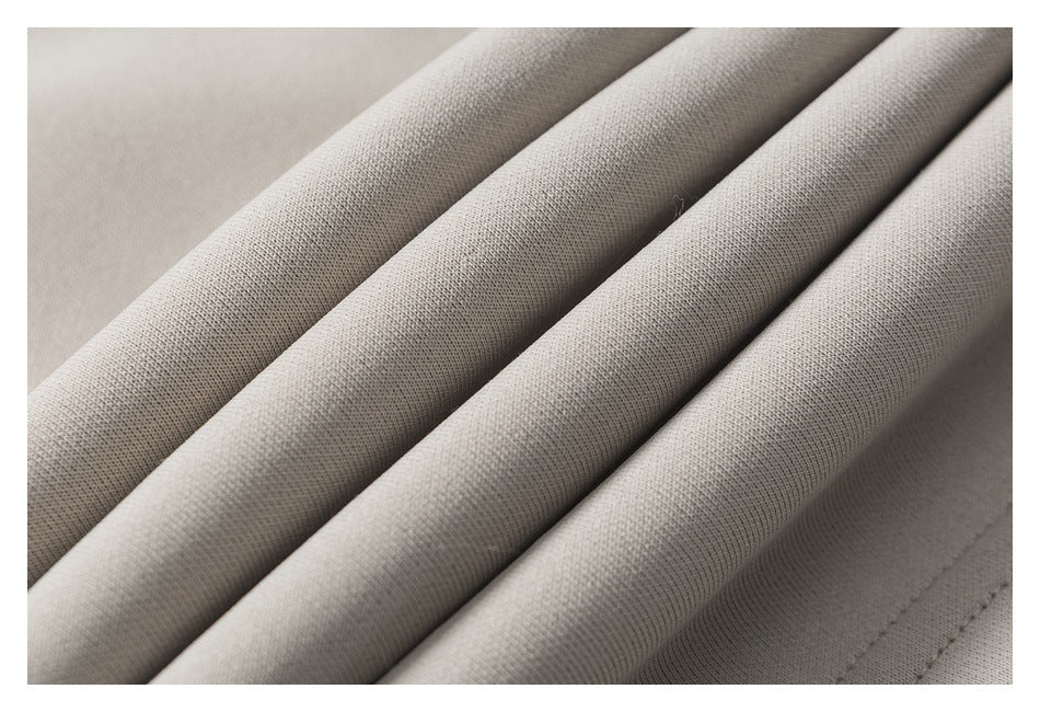 Close-up of light beige fabric arranged in folds, showing its fine surface texture and stitching.