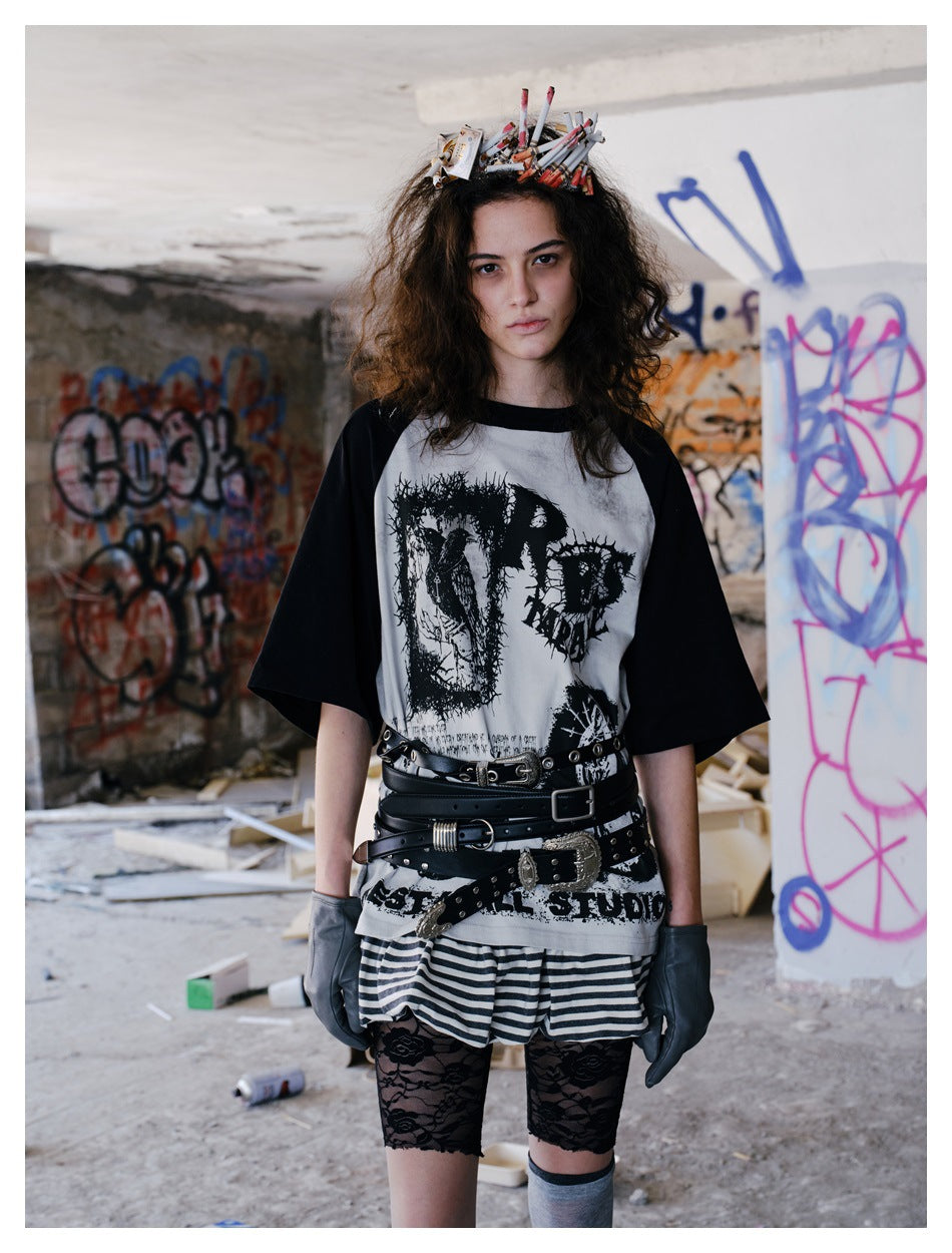 Model wearing the off-white raglan graphic T-shirt with black sleeves, belts and a striped skirt in a graffiti room