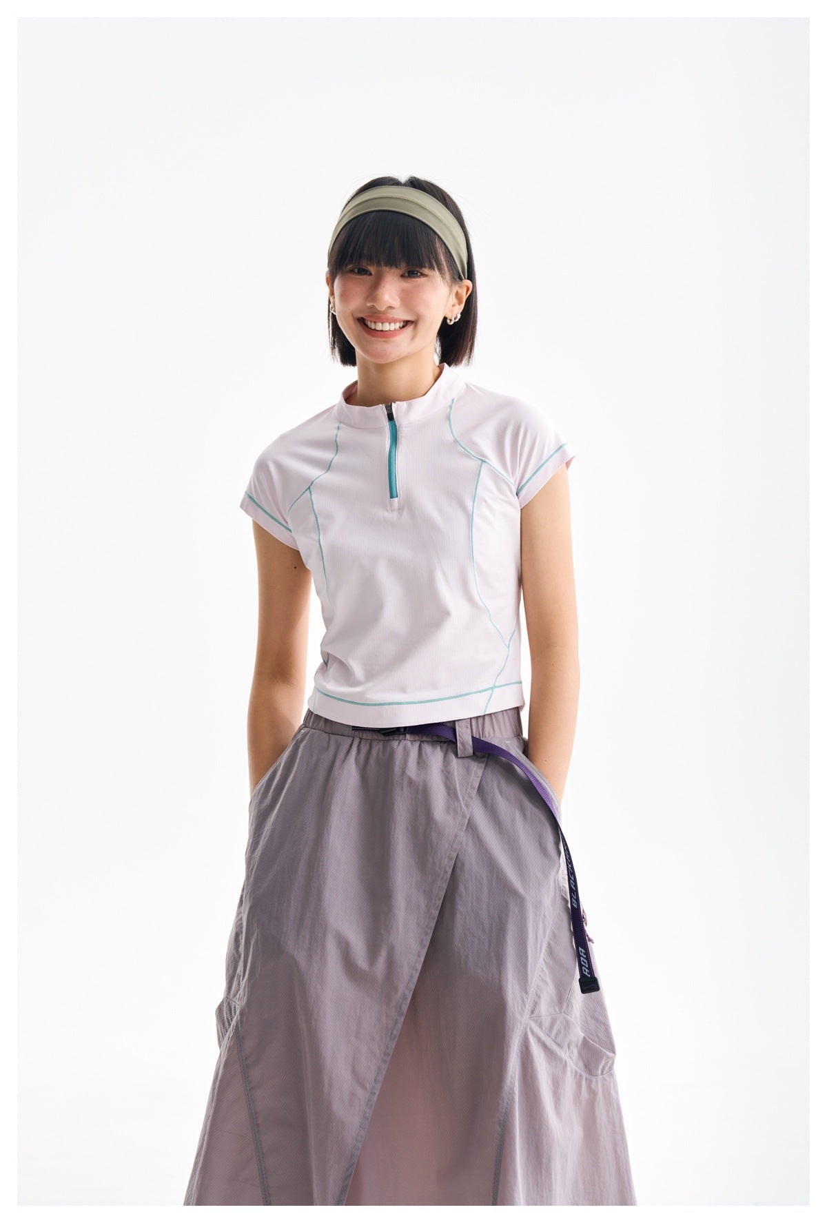 Front view of a model wearing a white zip-neck top with teal seam accents and a gray-lilac wrap skirt.