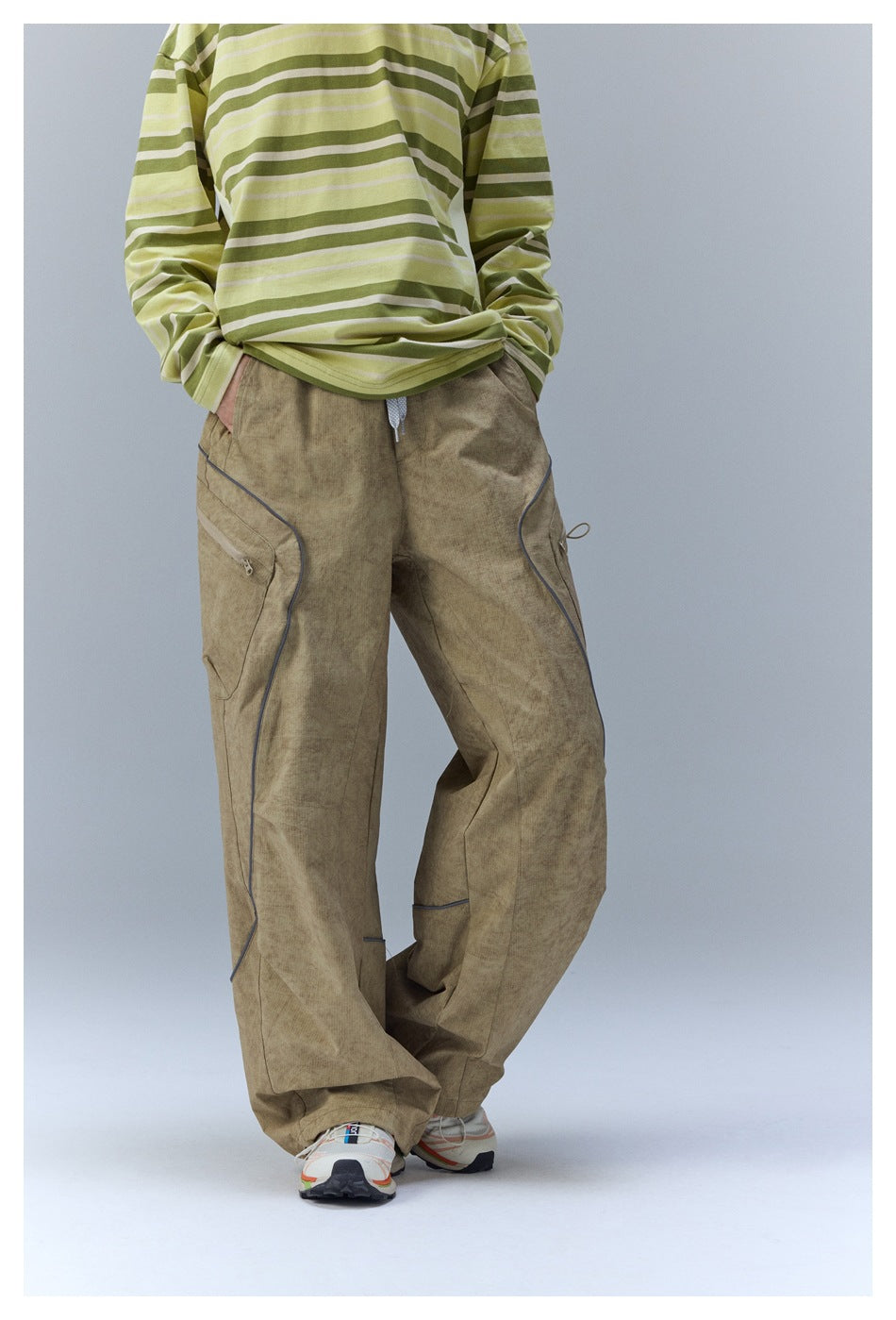 Front view of loose khaki cargo pants with curved dark piping, zip pockets, and a drawstring waist.