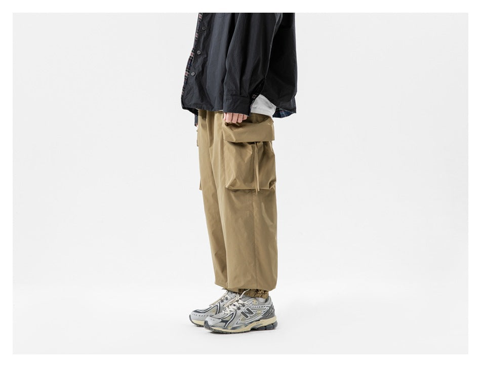 Side view of a model wearing loose tan cargo pants with a large flap cargo pocket.