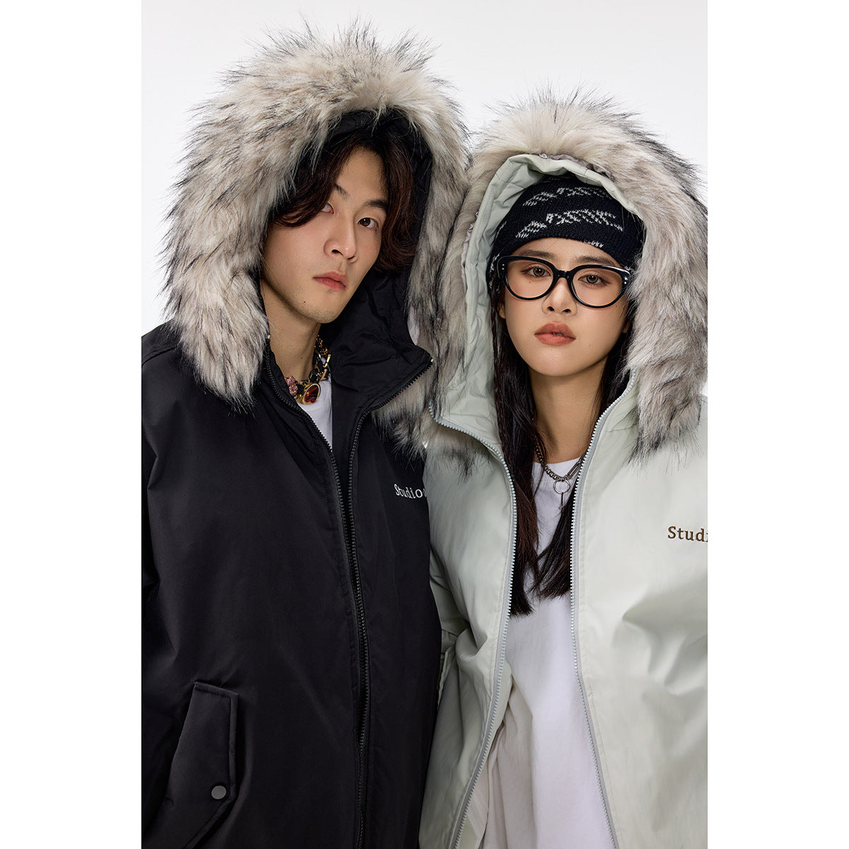 Two models wearing black and pale mint hooded jackets with oversized gray faux-fur trim.
