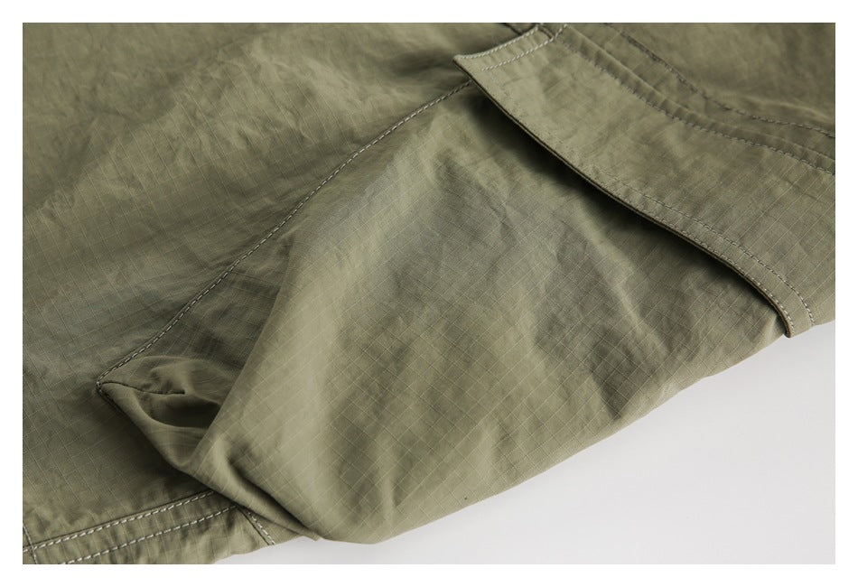 Close-up of olive shorts showing ripstop fabric, reinforced stitching, and a folded pocket flap.
