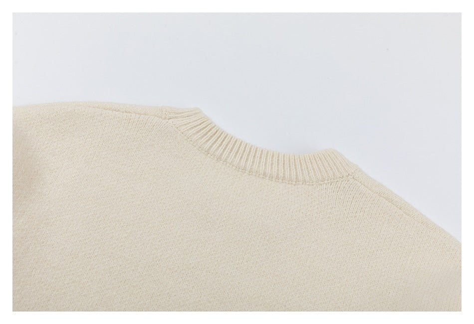 Close-up of a cream knit sweater showing its ribbed crew neckline and shoulder seam.