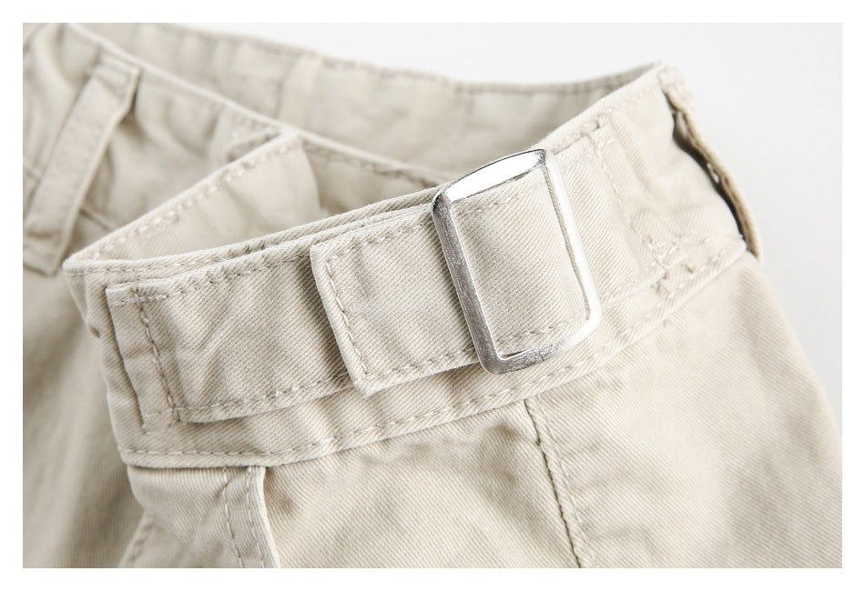 Close-up of the beige trousers' waistband and rectangular metal buckle on an adjustable side tab.