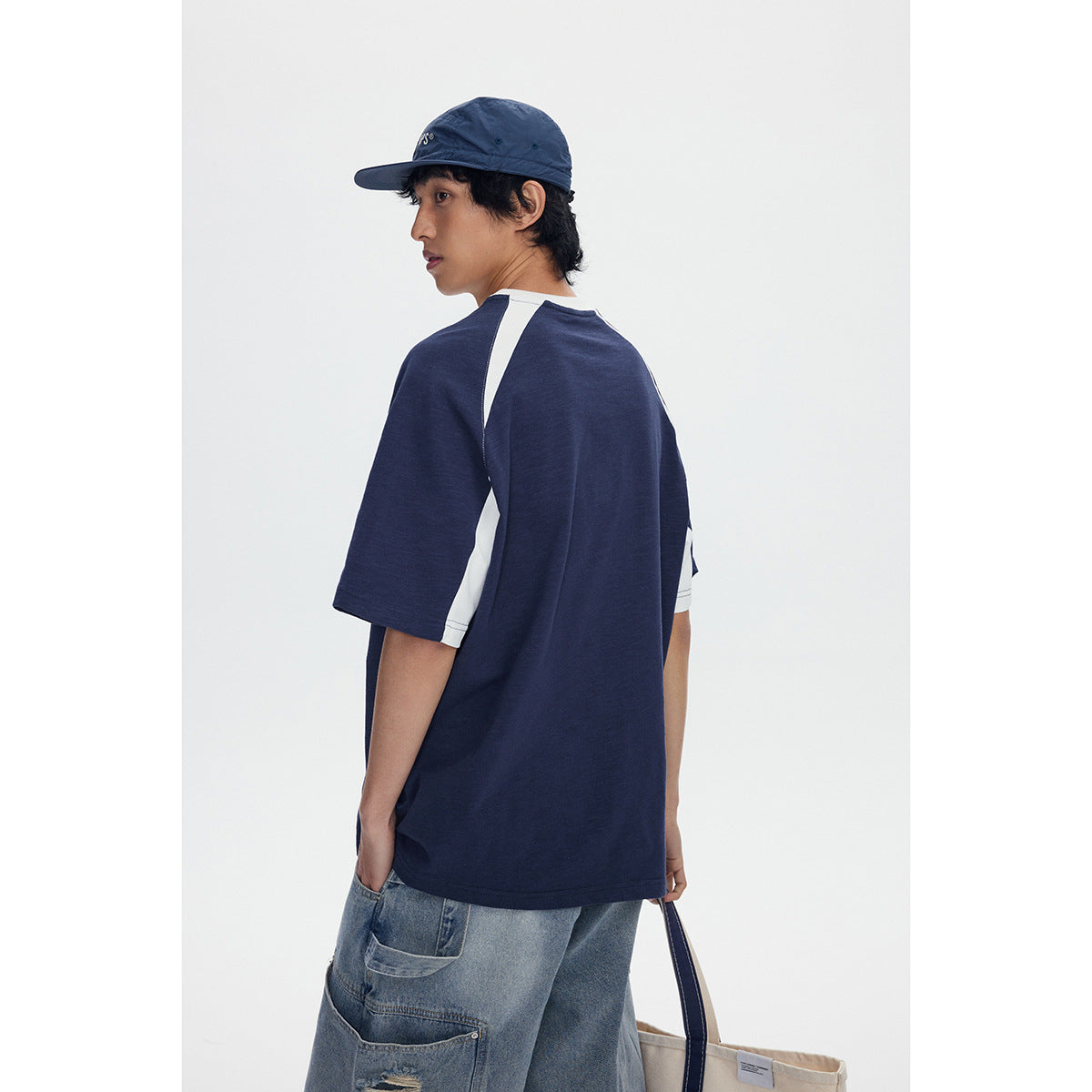 Rear view of a model wearing a navy T-shirt with white raglan and side panels.