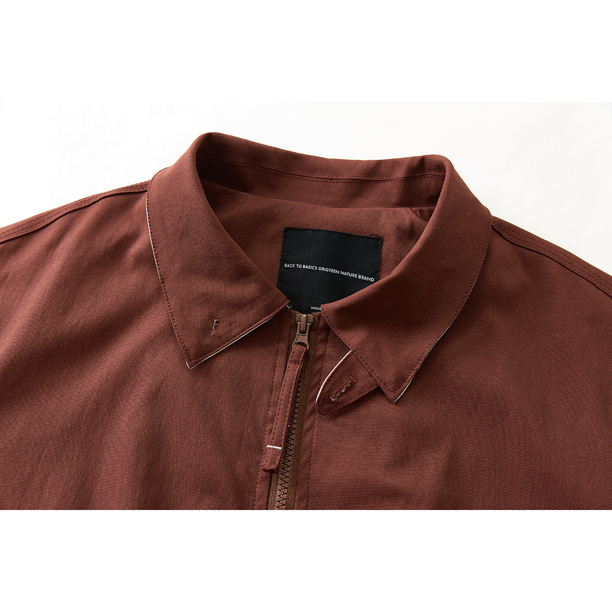 Close-up of a rust-brown jacket's pointed collar, front zipper and black inner neck label.