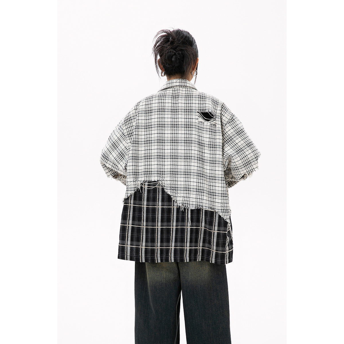 Rear view of a model wearing an oversized layered plaid shirt with a frayed hem and dark wide-leg jeans.
