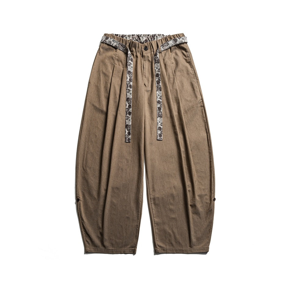 Light brown wide-leg trousers flat lay with a paisley-print tie belt and button tabs at the hems