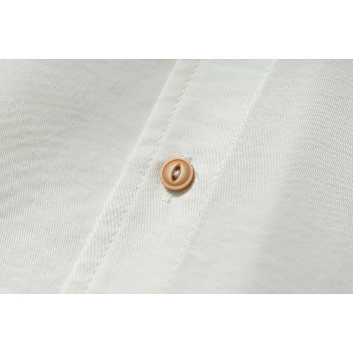 Close-up of a tan button and stitched placket on an off-white shirt.
