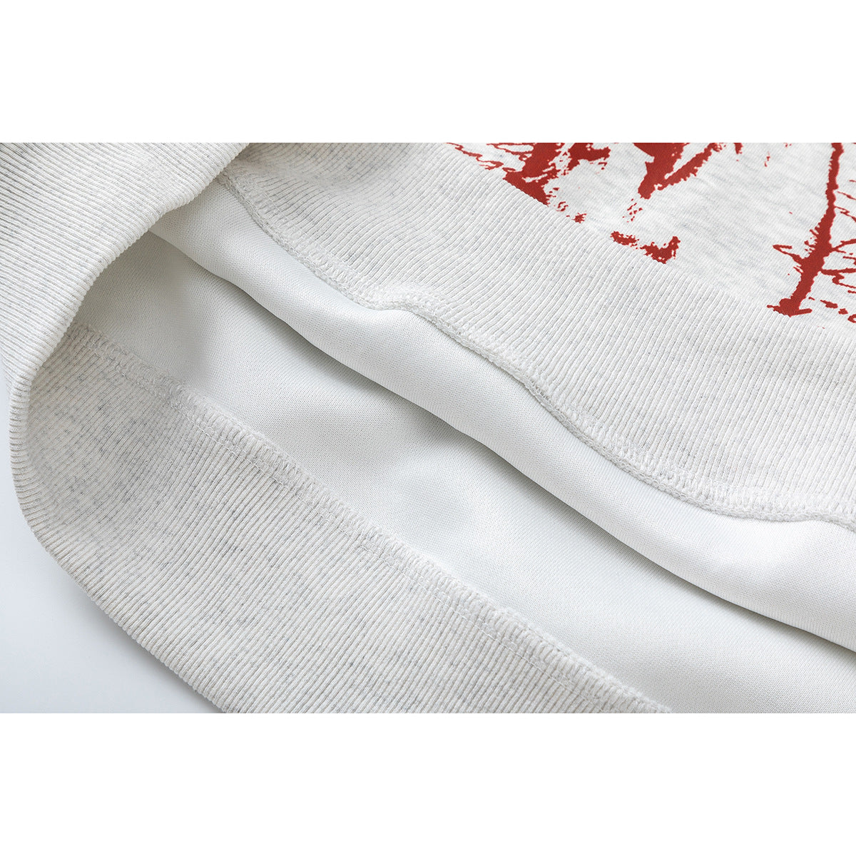 Close-up of the light gray sweatshirt's ribbed hem and interior stitching, with part of the red print visible.