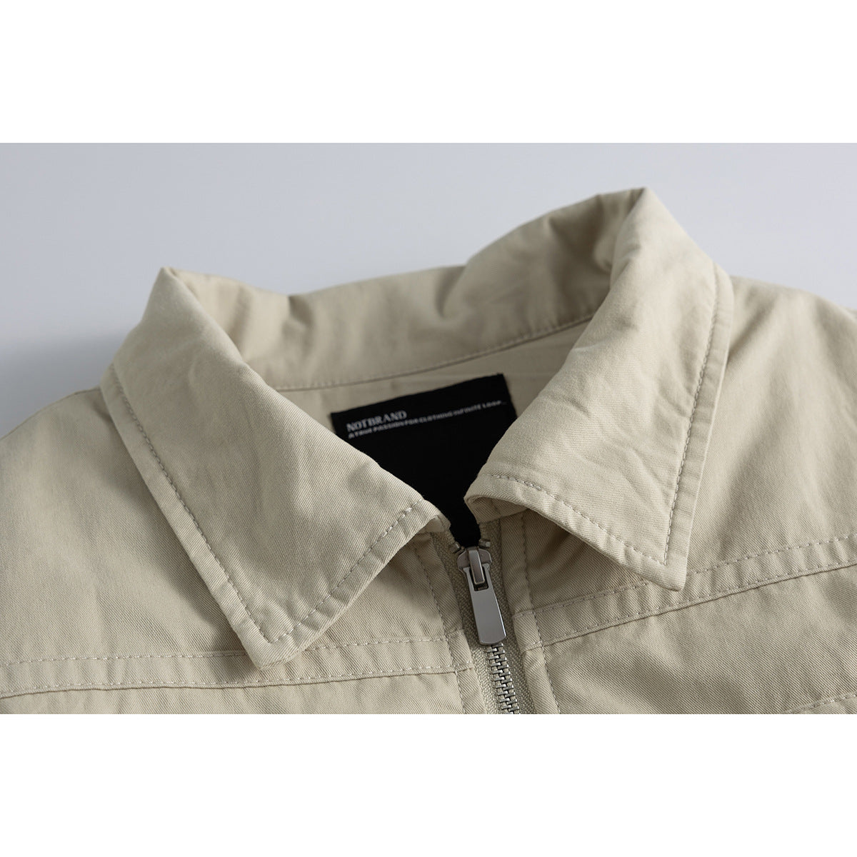 Close-up of a light beige jacket collar, front zipper, and inner neck label.