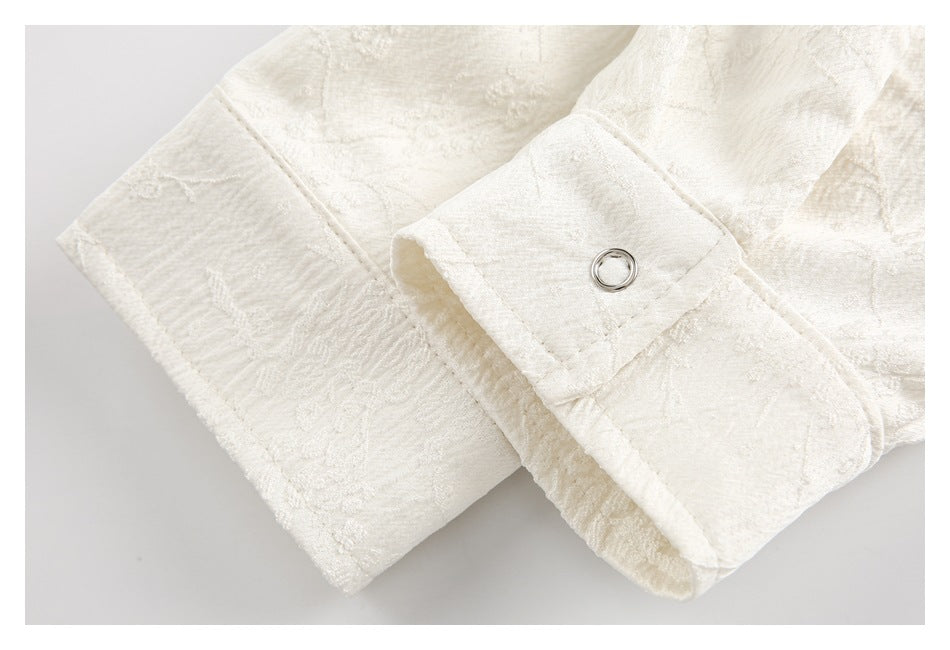 Close-up of an ivory textured garment cuff with a small metal eyelet and stitched edges.