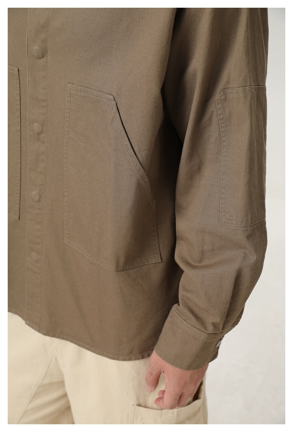 Close-up of a person wearing an olive-brown button-front shirt with large patch pockets and a sleeve pocket.