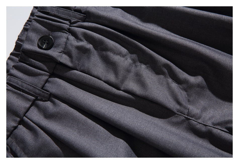 Close-up of dark charcoal trouser waistband with a black button, belt loop, and stitched fly area.