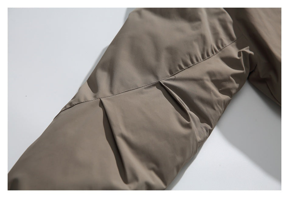 Close-up of a taupe garment sleeve with a diagonal seam and folded pleat detail.