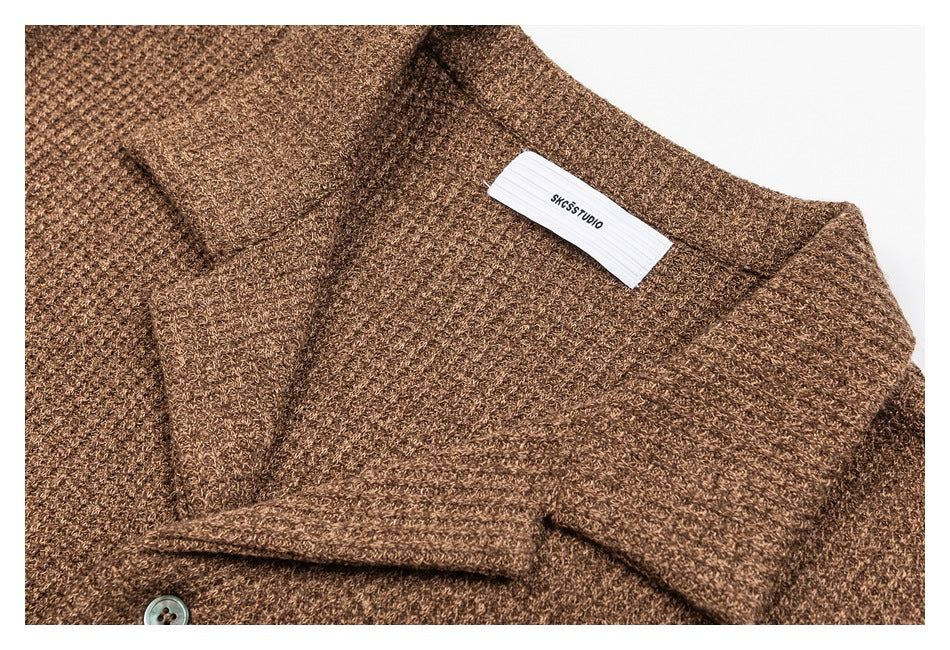 Close-up of a brown knit cardigan's shawl collar, button, textured stitch, and sewn neck label.