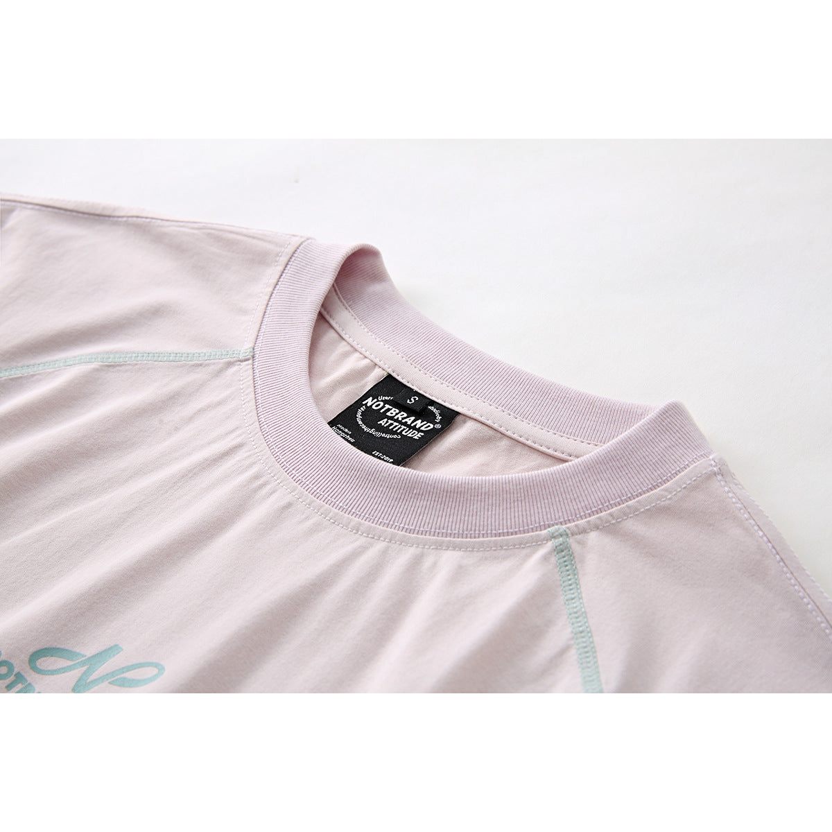 Close-up of a pale blush T-shirt collar with aqua stitching, a partial chest graphic, and a black neck label.