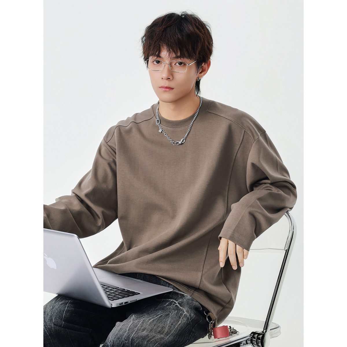 Seated model wearing an oversized taupe long-sleeve crewneck top with seamed shoulders.