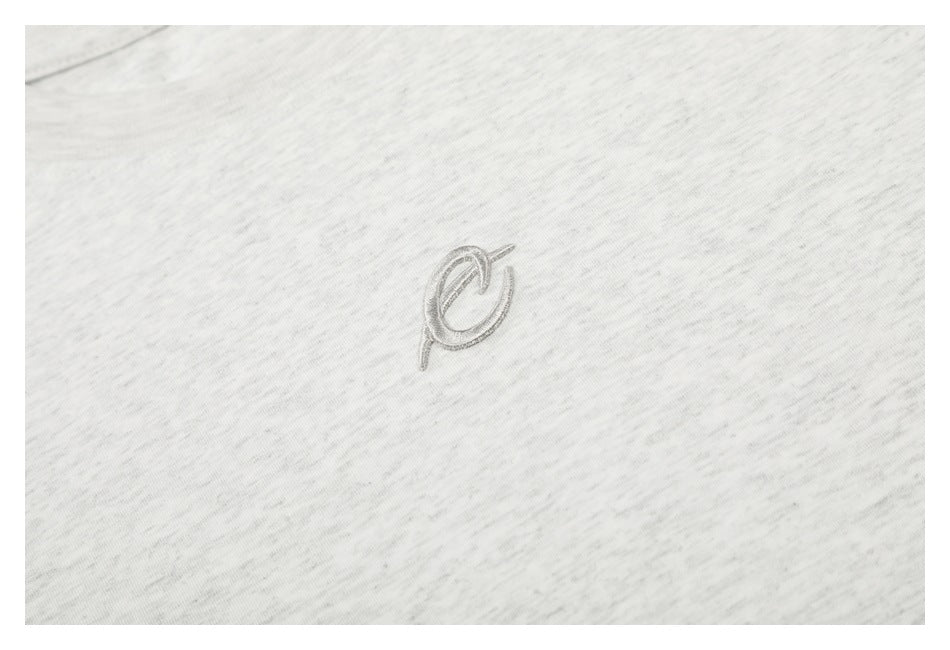 Small tonal embroidered emblem on light gray marled T-shirt fabric.