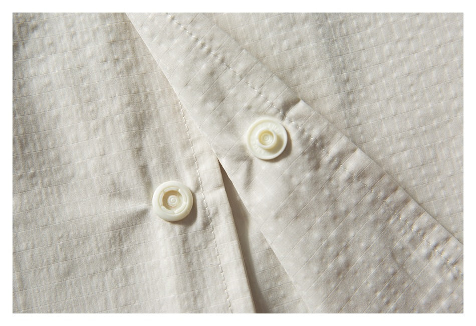 Close-up of an ivory shirt placket with two round buttons and subtle woven stripes.