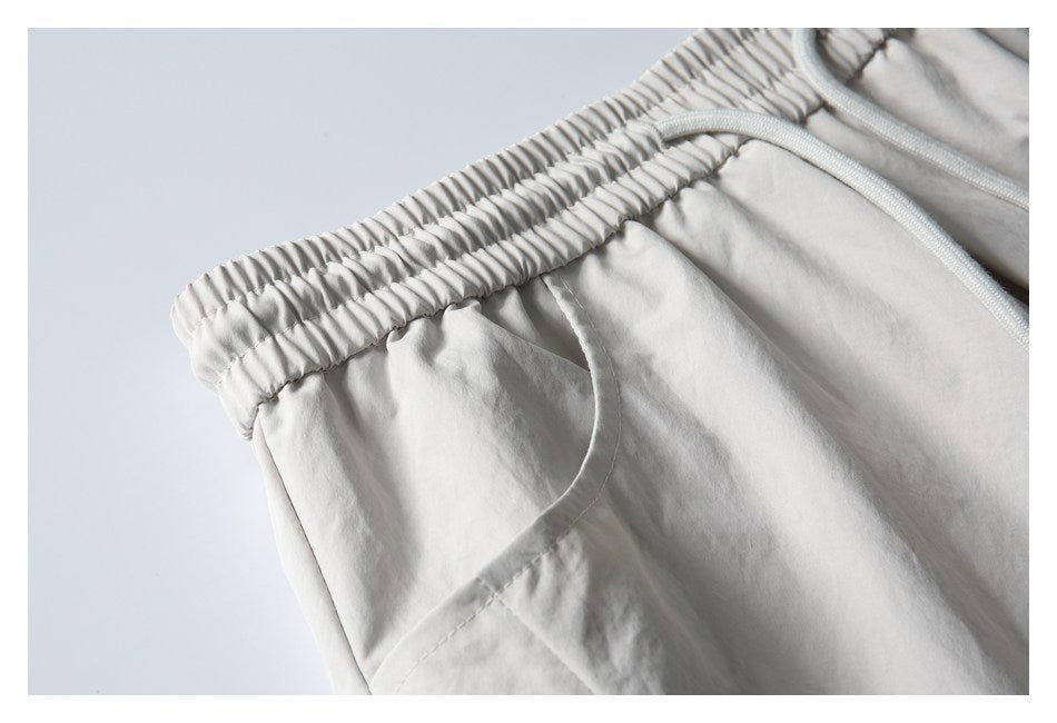 Close-up of light gray shorts showing the elastic waistband and curved side pocket opening.