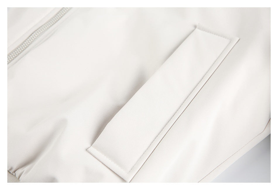 Close-up of a rectangular pocket flap on an ivory jacket beside part of the zipper.