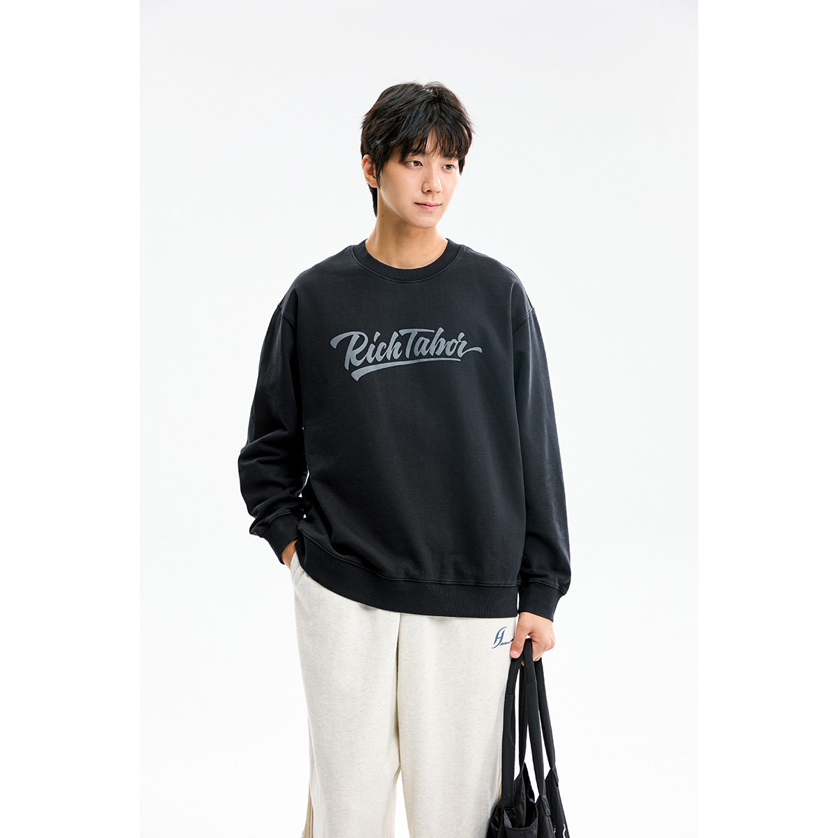 Model wearing a black crewneck sweatshirt with gray script print and light gray sweatpants.