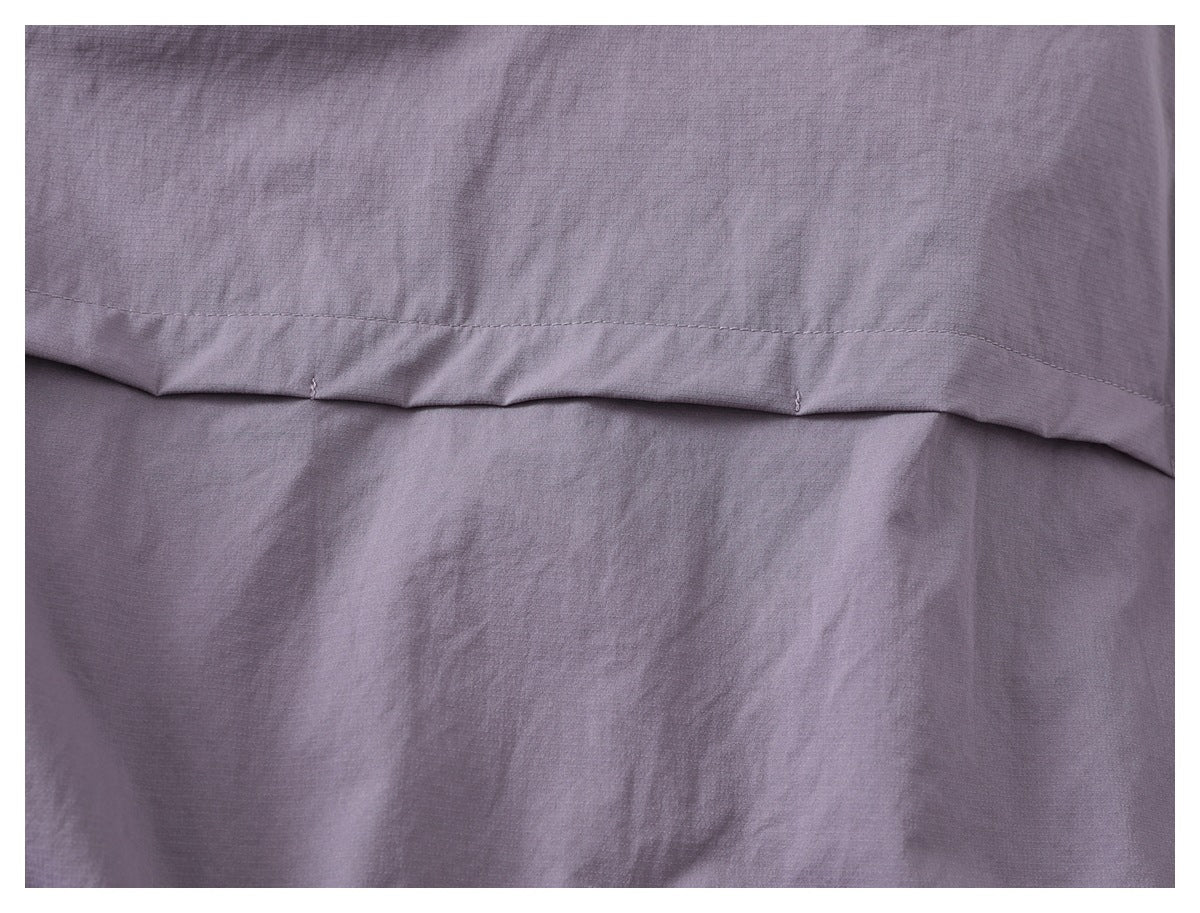Close-up of muted mauve-gray fabric with a curved stitched seam and a small loose thread.