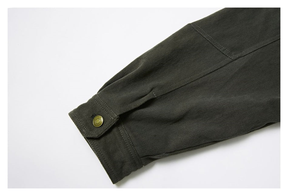 Close-up of a dark olive garment cuff with a brass-tone snap button and stitched seams.