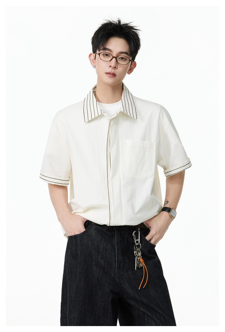 Man wearing an off-white short-sleeve shirt with striped collar and cuffs, chest pocket, over a white tee with black jeans