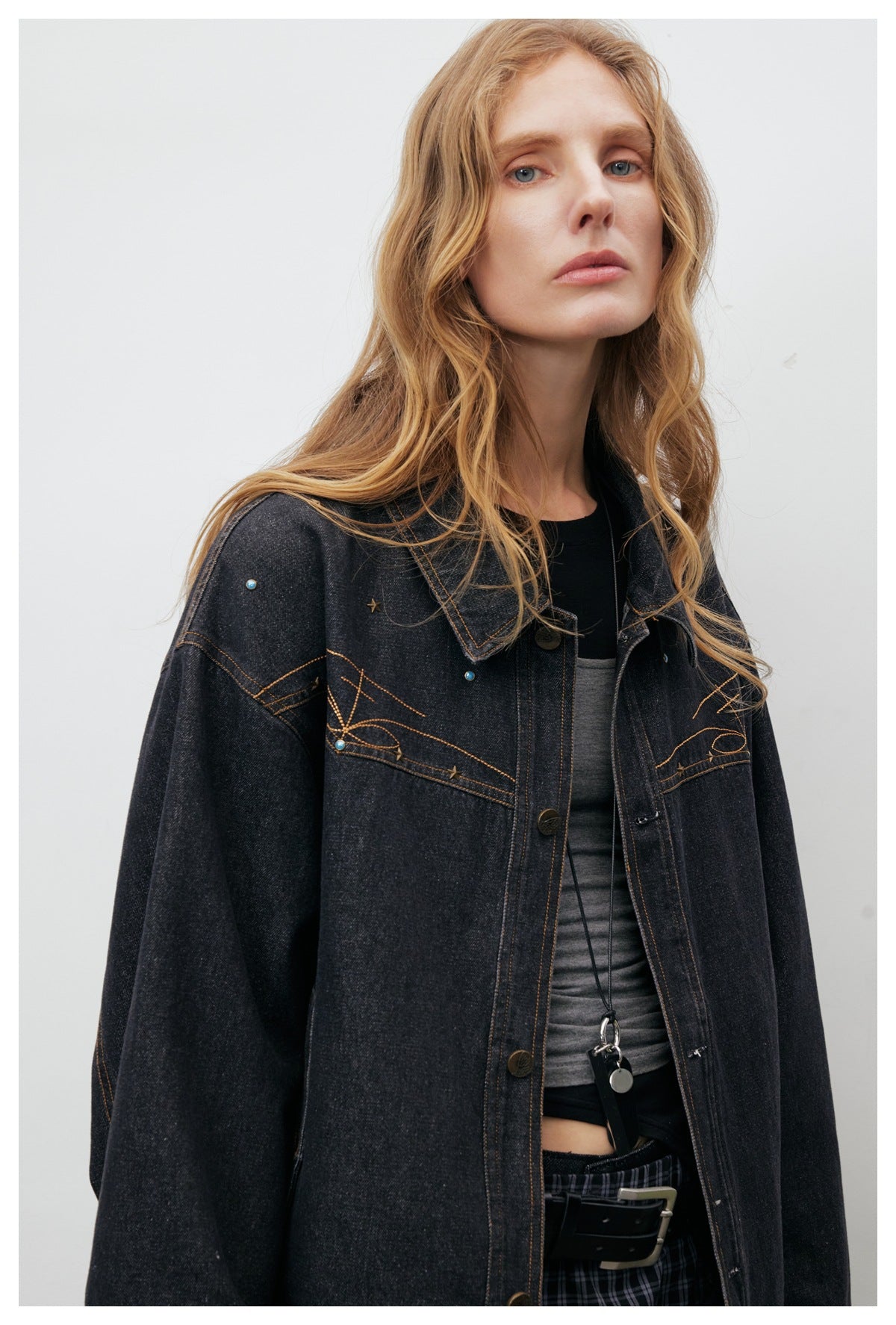 Close view of a model wearing a black denim jacket with tan stitched motifs and small blue accents.