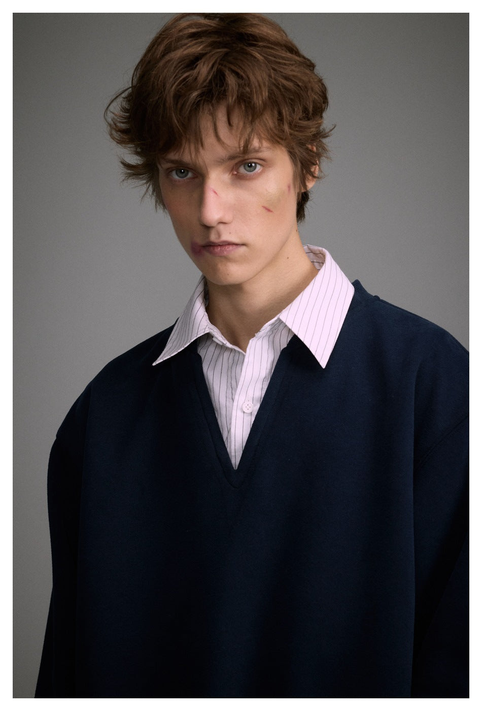 Model wearing a dark navy V-neck sweater over a white shirt with thin vertical stripes.