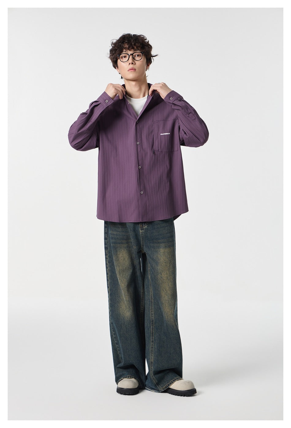 Model wearing a muted purple button-front shirt with a chest pocket and wide-leg faded blue jeans.