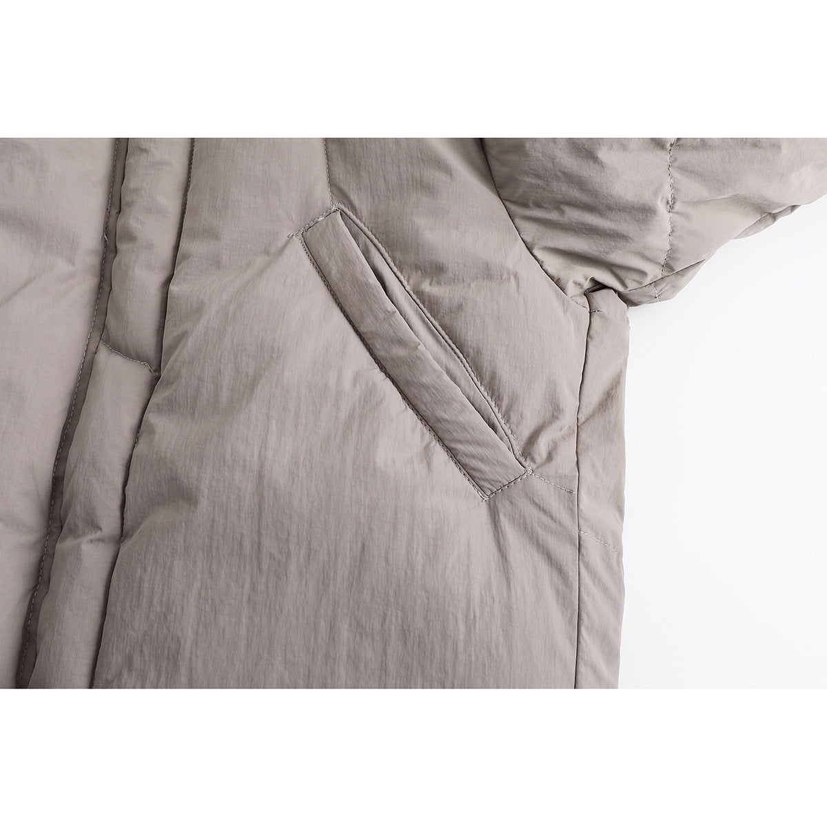 Close-up of a taupe padded jacket's angled welt pocket and quilted side panel.