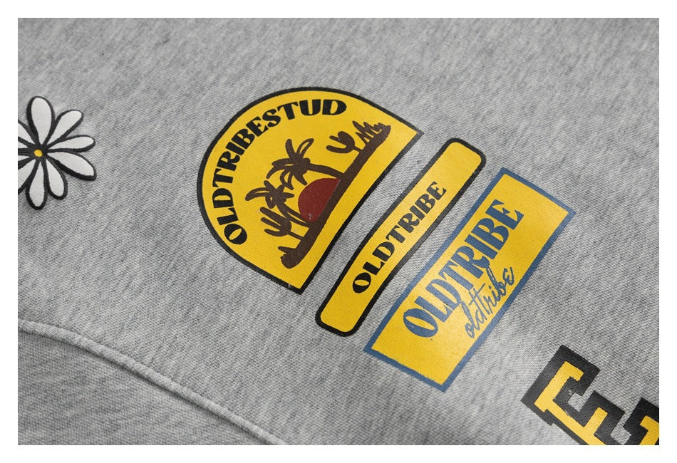 Close-up of yellow and blue Oldtribe graphics and a white daisy on heather-gray fabric.
