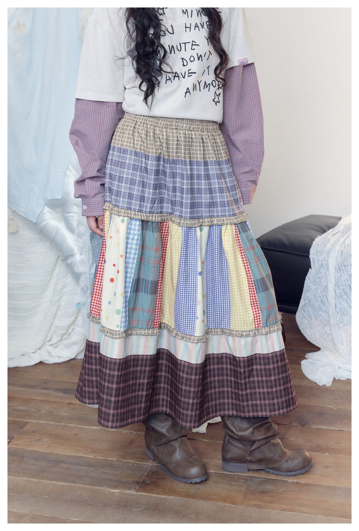 Close view of a model wearing a tiered patchwork skirt with an elastic waist, colorful panels, ruffled seams, and dark plaid
