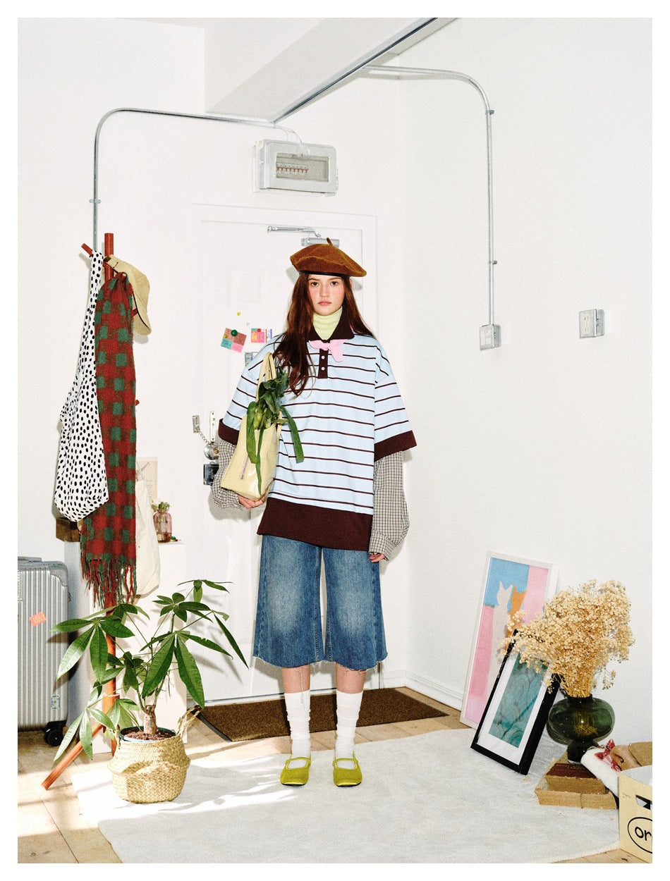 Front view of a model wearing an oversized light blue striped top with a dark brown collar, hem and cuffs over checked