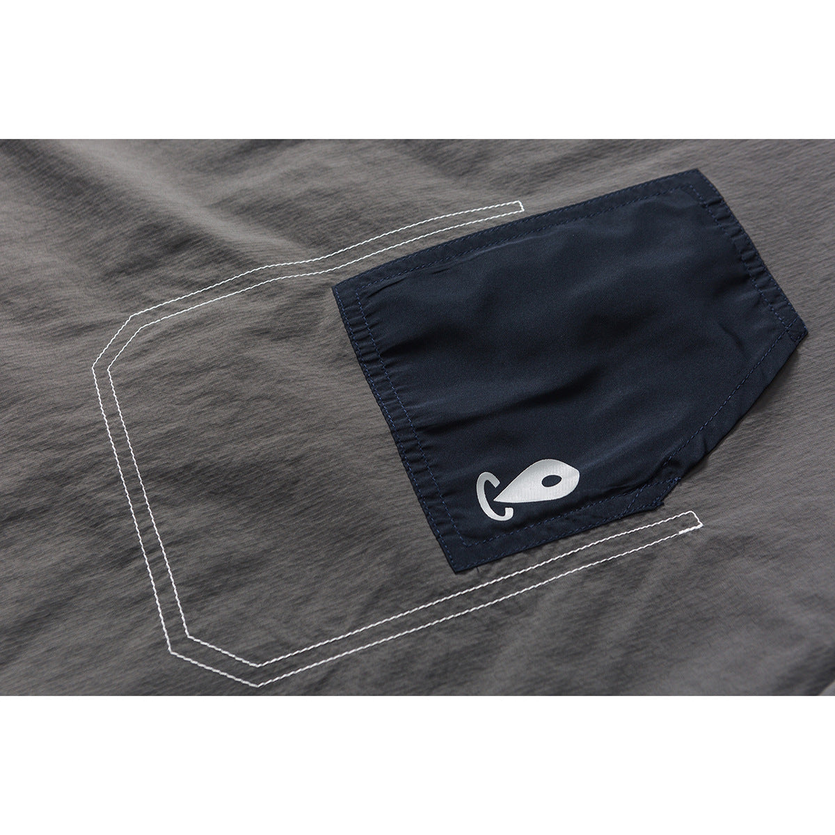 Close-up of a charcoal gray top with a navy pocket, white fish symbol, and contrast stitching.