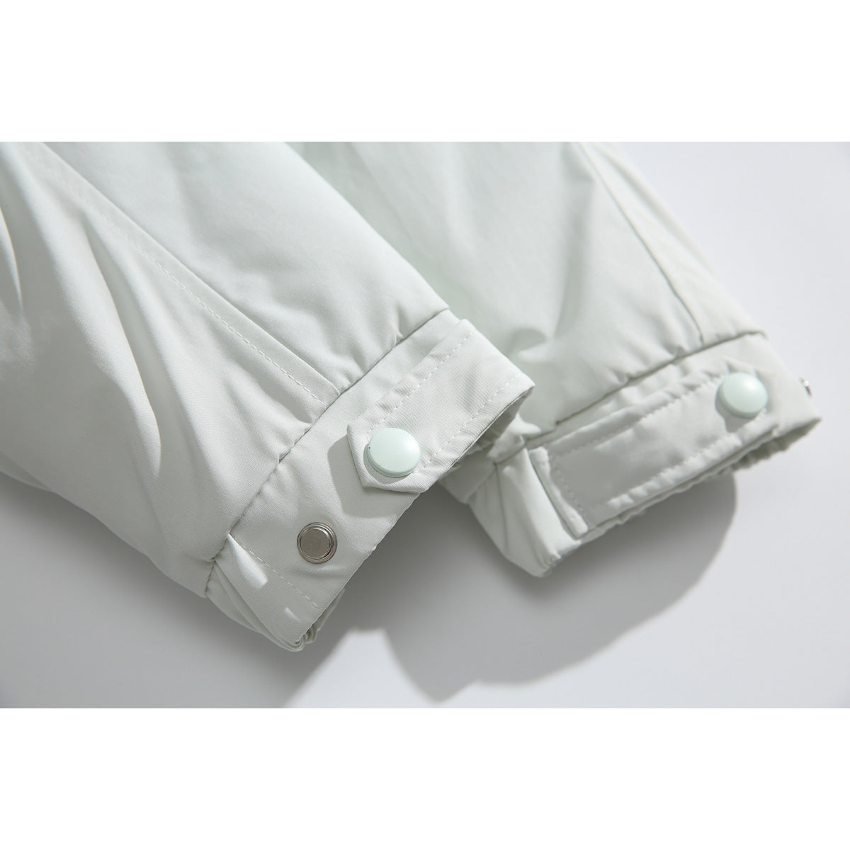 Close-up of a white jacket sleeve cuff with snap-button tabs and stitching.