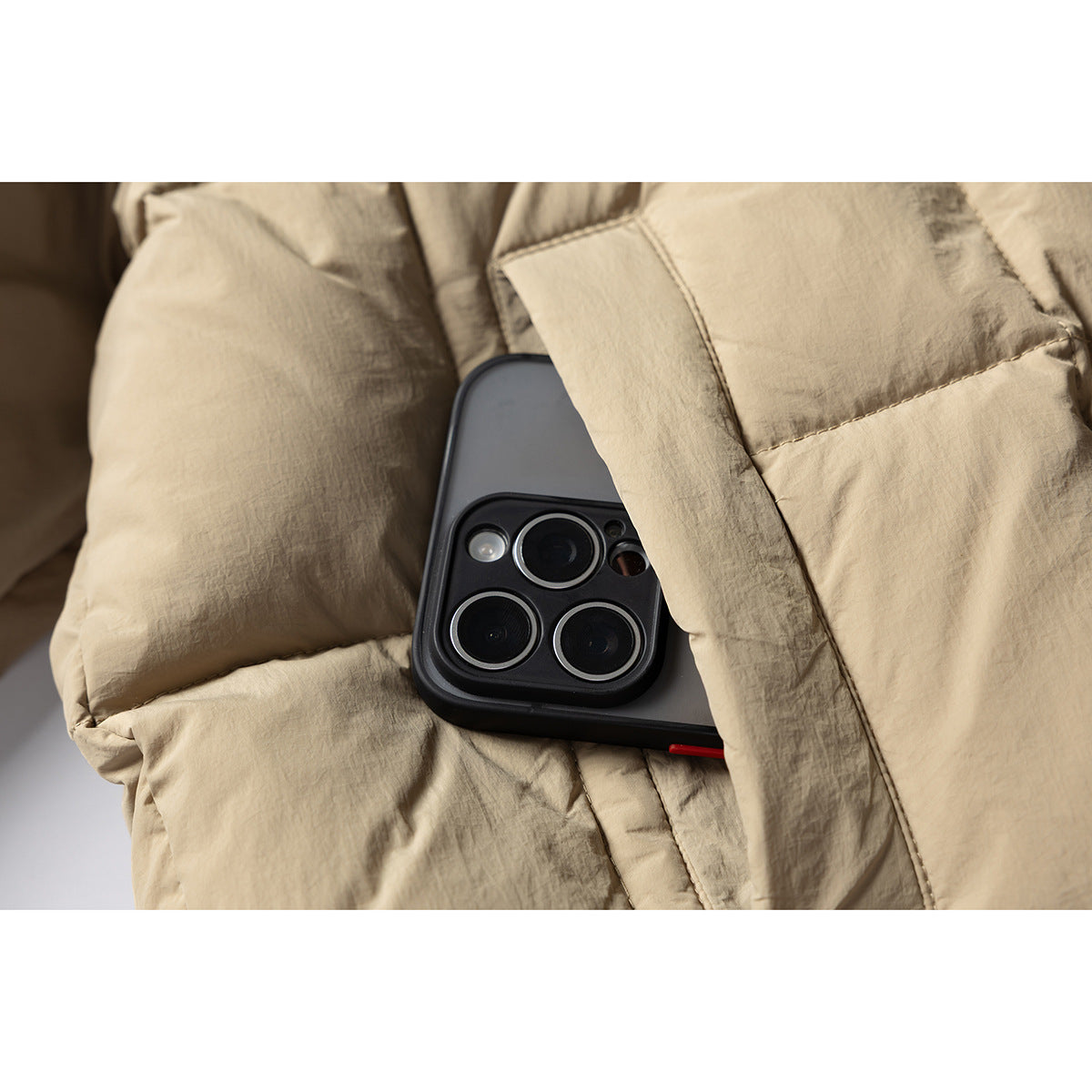 A black smartphone is partly tucked into a pocket on a tan quilted jacket.