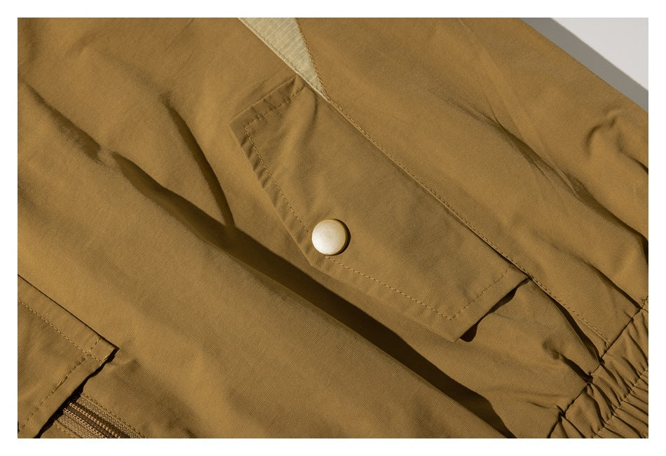Close-up of a mustard-brown garment showing a flap pocket with a light-colored snap and a gathered edge.