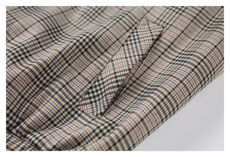 Close-up of a beige, black, and blue plaid garment showing a diagonal pocket opening and stitched seams.