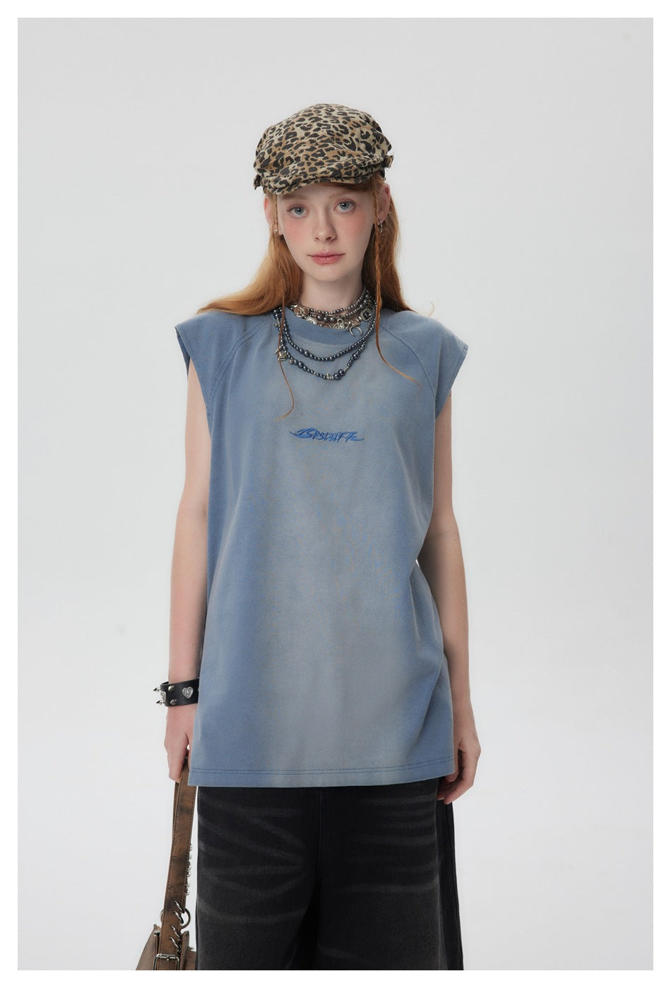 Front view of a model wearing a faded blue sleeveless shirt with small chest lettering.