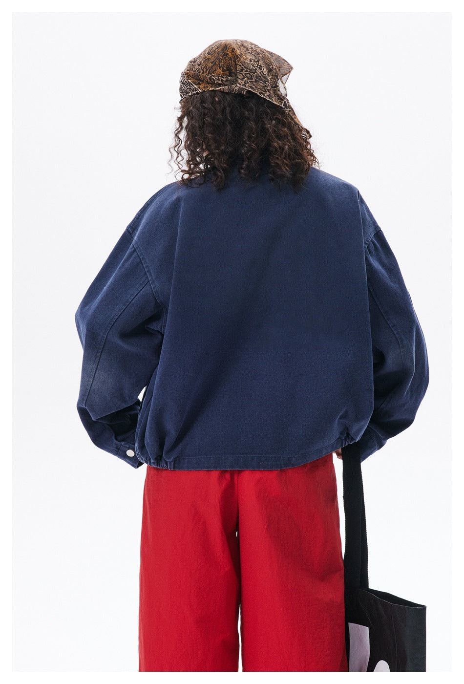 Back view of a person wearing an oversized dark navy jacket with dropped shoulders and an elasticated hem.