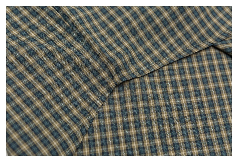 Close-up of a plaid shirt seam and overlapping fabric in blue, tan, and cream.