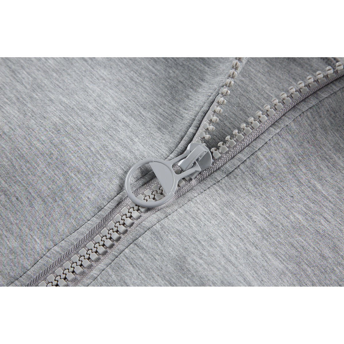 Close-up of the light gray jacket's chunky zipper and circular pull on heathered fabric.