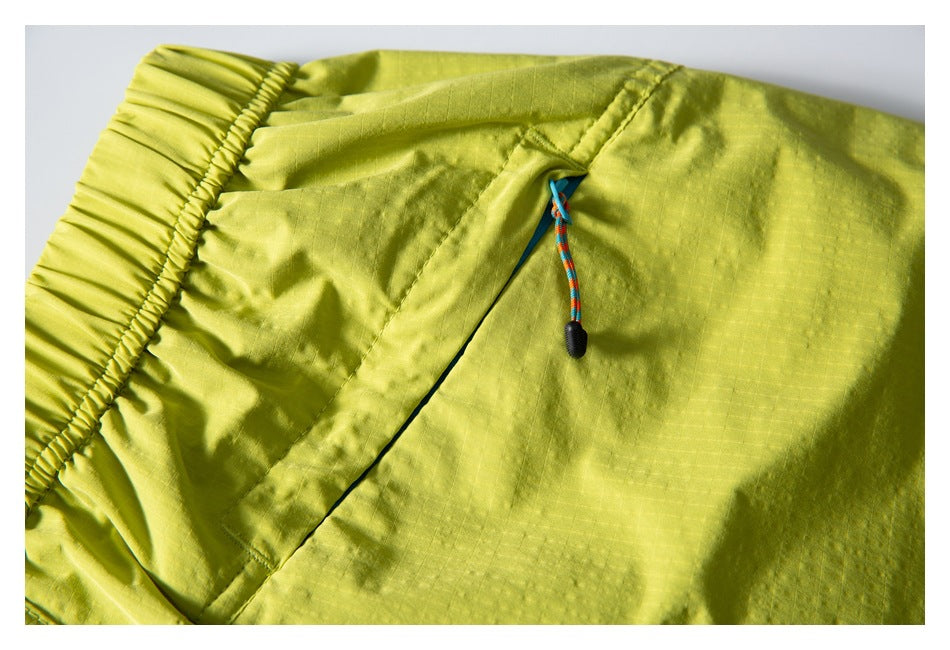 Close-up of lime green shorts showing an elastic waistband, angled pocket, and multicolored drawcord.