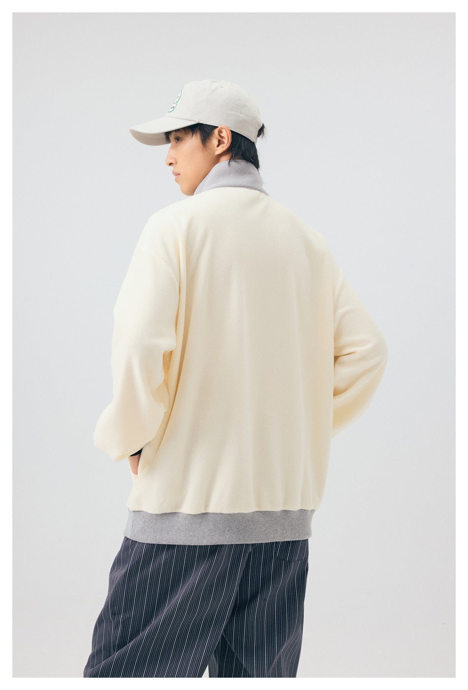 Model wearing the cream pullover, shown from the back with a gray collar and hem.