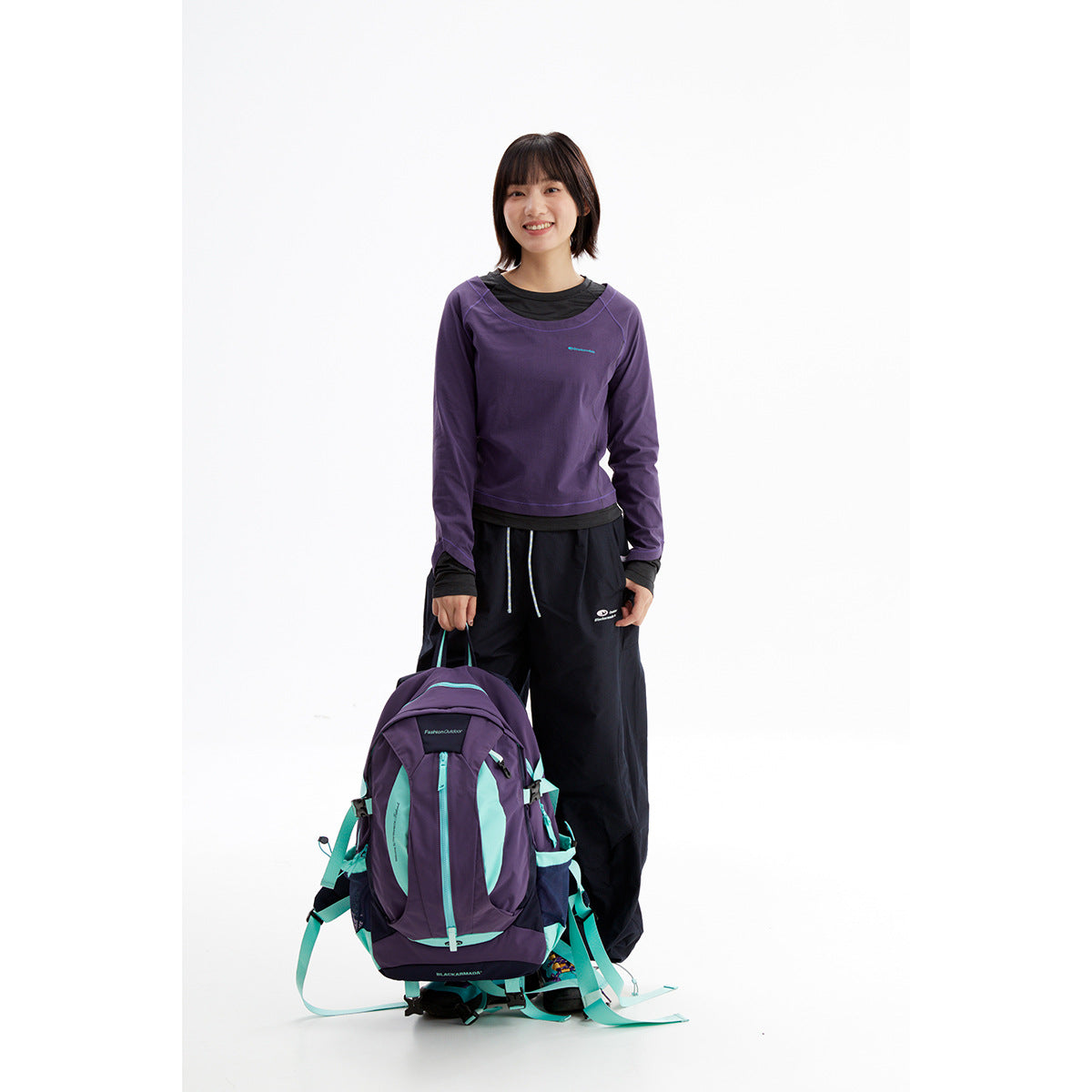 Front view of a model wearing a purple long-sleeve top over a black shirt with black trousers.